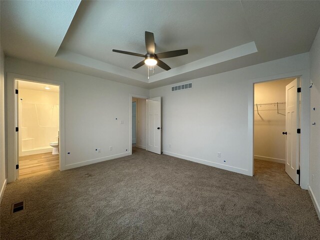 unfurnished bedroom with carpet flooring, a walk in closet, a raised ceiling, ceiling fan, and a closet