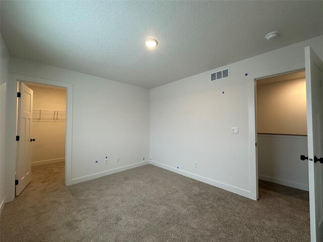 unfurnished bedroom with carpet flooring, a textured ceiling, a spacious closet, and a closet