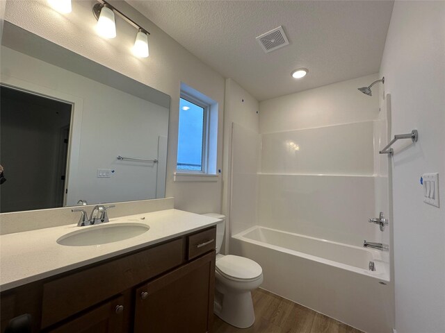 full bathroom featuring vanity, bathing tub / shower combination, hardwood / wood-style flooring, toilet, and a textured ceiling