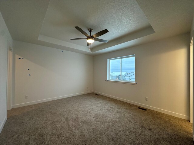 spare room featuring carpet, ceiling fan, a textured ceiling, and a tray ceiling