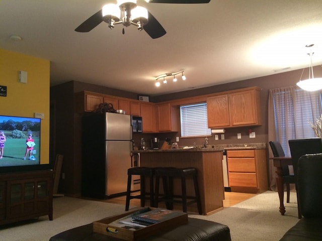 kitchen with ceiling fan, hanging light fixtures, stainless steel fridge, a kitchen bar, and light carpet