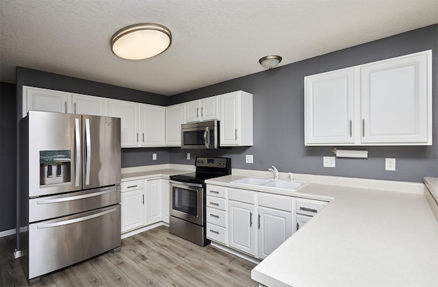 kitchen with sink, stainless steel appliances, light hardwood / wood-style flooring, a textured ceiling, and white cabinets