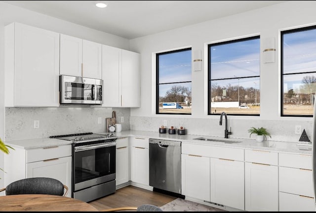 kitchen featuring white cabinets, appliances with stainless steel finishes, a sink, light countertops, and backsplash