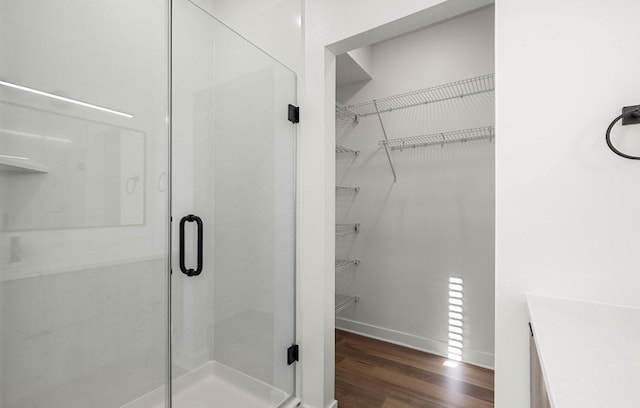 bathroom with a stall shower, a spacious closet, baseboards, and wood finished floors