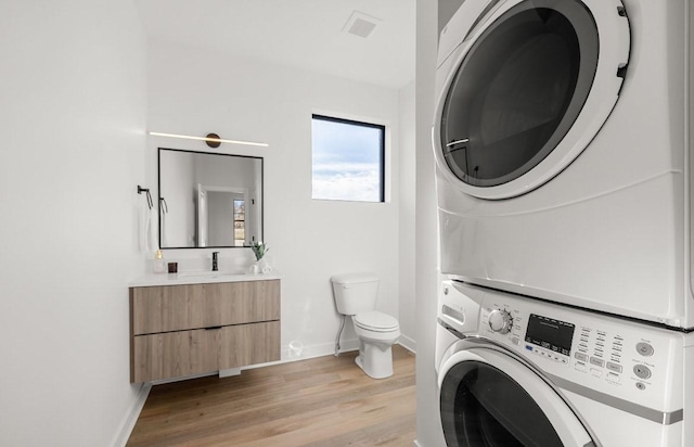 laundry area with visible vents, baseboards, light wood-style flooring, stacked washing maching and dryer, and a sink