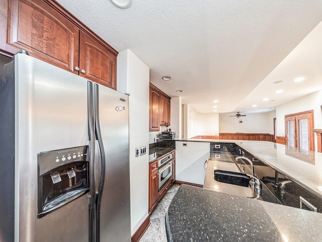 kitchen with ceiling fan, sink, stainless steel appliances, kitchen peninsula, and dark stone counters