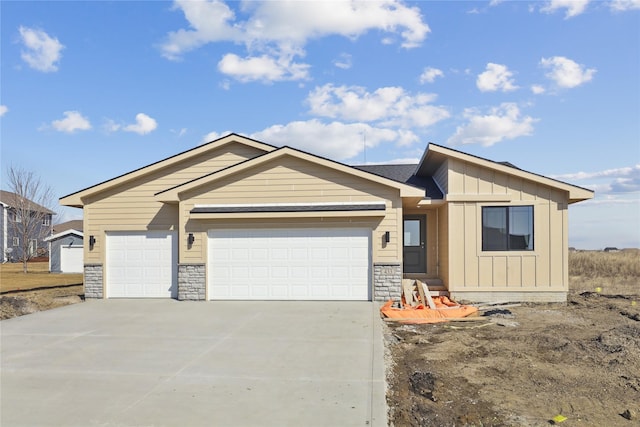 view of front of property featuring an attached garage, stone siding, board and batten siding, and concrete driveway