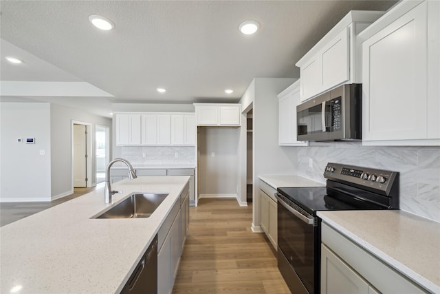 kitchen with recessed lighting, backsplash, light wood-style flooring, appliances with stainless steel finishes, and a sink