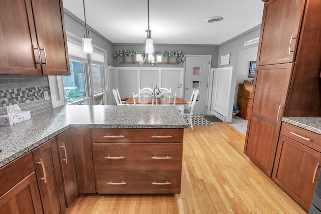 kitchen featuring decorative light fixtures, light wood-type flooring, backsplash, and kitchen peninsula