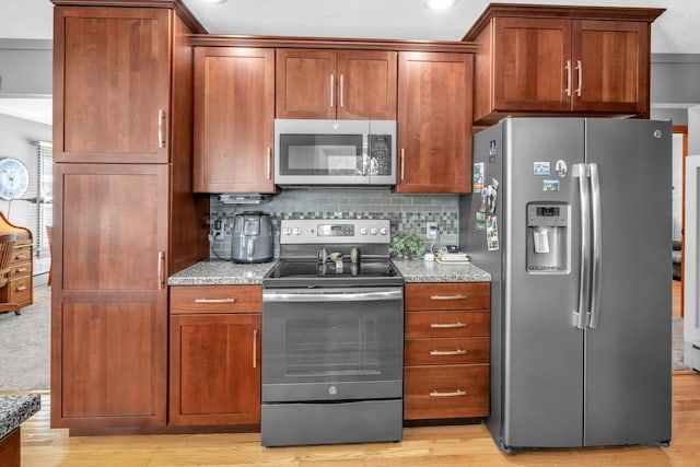 kitchen featuring decorative backsplash, stainless steel appliances, light stone counters, and light hardwood / wood-style flooring