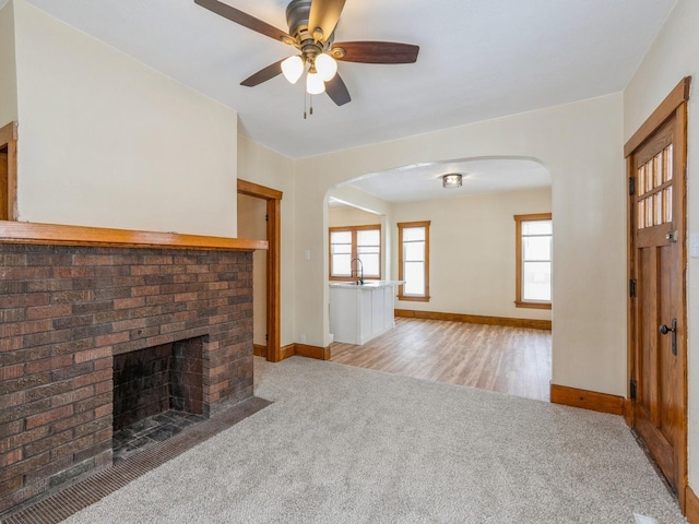 unfurnished living room featuring a fireplace, light colored carpet, ceiling fan, and sink