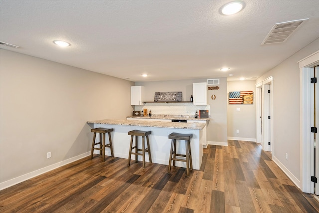 kitchen featuring white cabinetry, a kitchen bar, dark wood-type flooring, and decorative backsplash