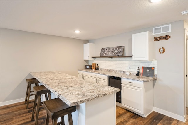 kitchen featuring a kitchen bar, white cabinetry, dark wood-type flooring, light stone counters, and beverage cooler