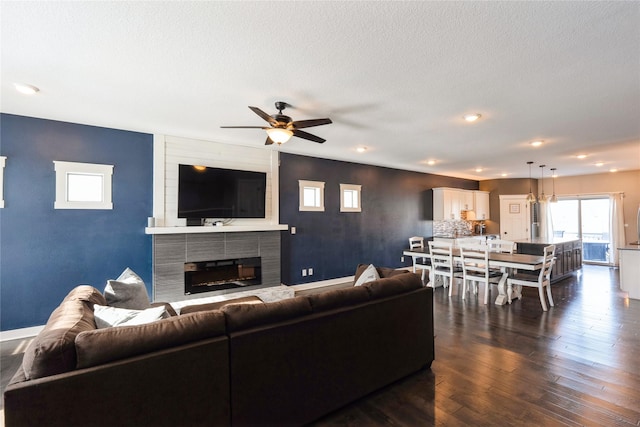 living room featuring ceiling fan, a textured ceiling, a tile fireplace, and dark hardwood / wood-style flooring