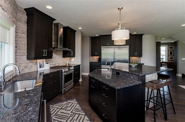 kitchen with sink, premium appliances, a kitchen island with sink, and wall chimney range hood