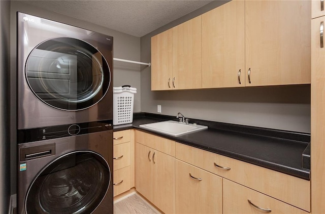 washroom with cabinets, sink, stacked washer and dryer, light wood-type flooring, and a textured ceiling