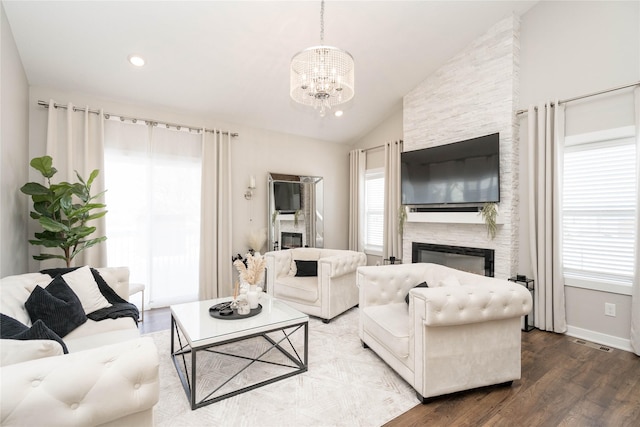 living room featuring vaulted ceiling, a stone fireplace, wood-type flooring, and a chandelier