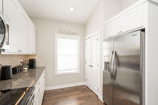 kitchen with dark stone countertops, white cabinets, stainless steel fridge, decorative backsplash, and stove