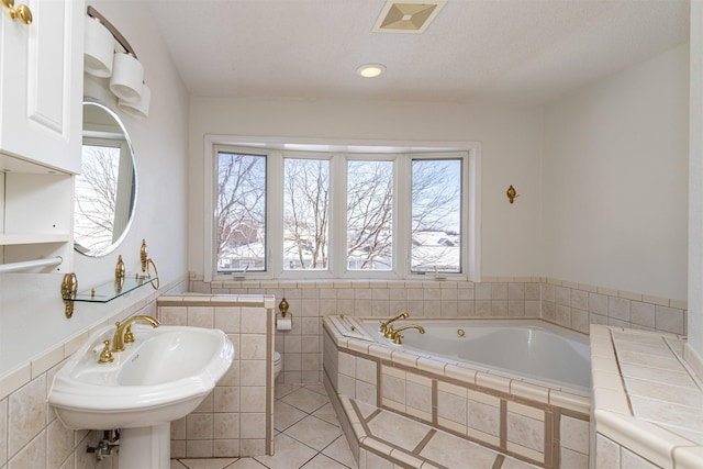 bathroom with toilet, sink, tile walls, tiled tub, and tile patterned flooring