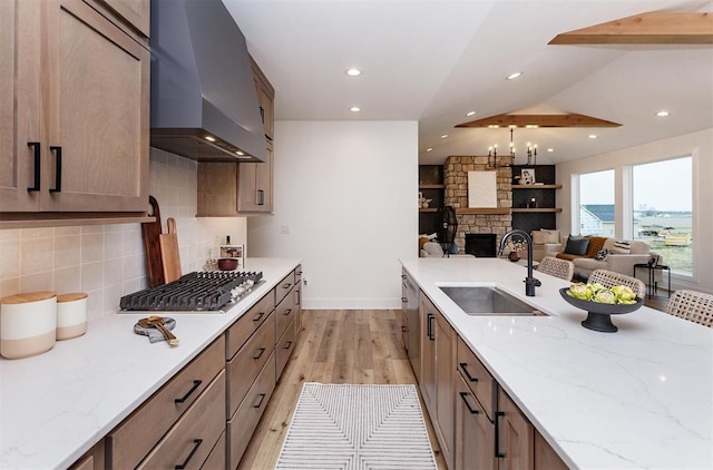 kitchen with sink, a stone fireplace, light stone countertops, and wall chimney exhaust hood