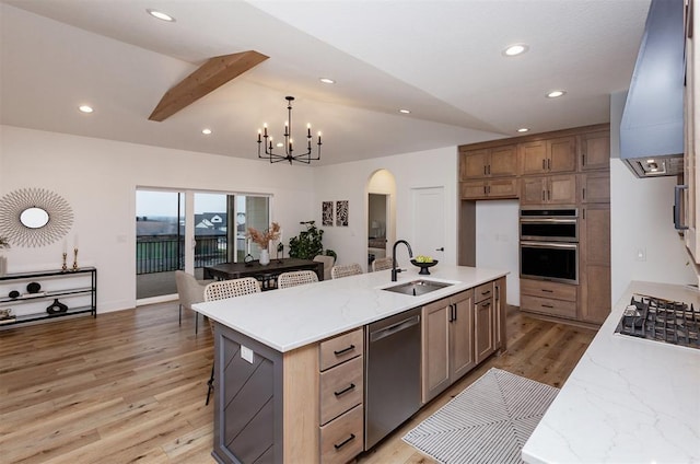 kitchen with sink, appliances with stainless steel finishes, an inviting chandelier, a large island with sink, and light wood-type flooring