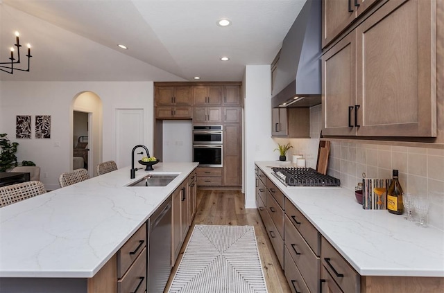 kitchen featuring sink, stainless steel appliances, an island with sink, and wall chimney exhaust hood