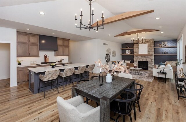 dining space with lofted ceiling with beams, a stone fireplace, sink, light wood-type flooring, and a chandelier