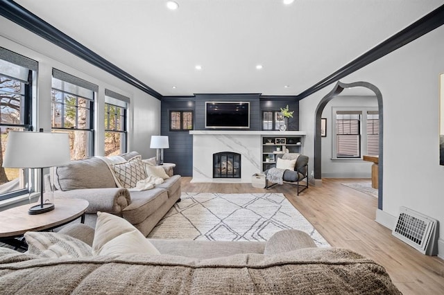 living room featuring built in shelves, crown molding, a fireplace, and light wood-type flooring