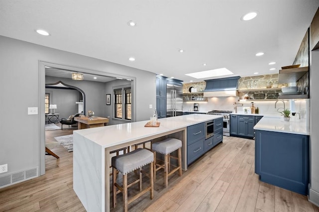 kitchen with a kitchen breakfast bar, a skylight, blue cabinets, high quality appliances, and light hardwood / wood-style floors