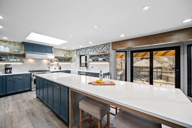 kitchen featuring a skylight, wall chimney exhaust hood, a kitchen breakfast bar, blue cabinets, and appliances with stainless steel finishes