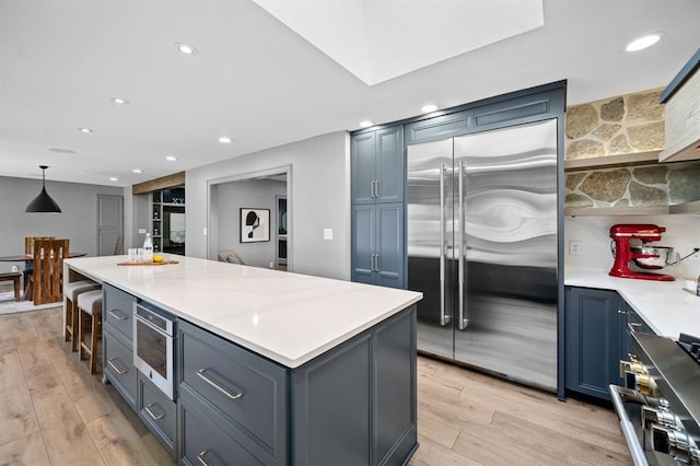 kitchen with pendant lighting, a center island, light wood-type flooring, and stainless steel built in refrigerator