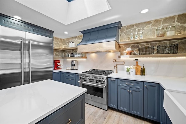 kitchen with blue cabinetry, high quality appliances, custom range hood, and backsplash