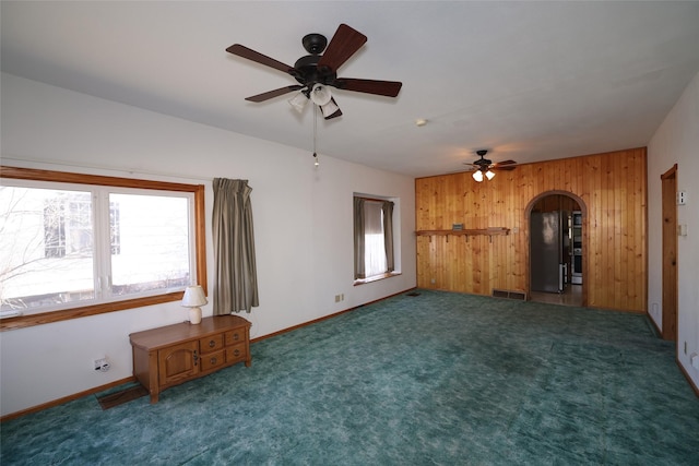 interior space with ceiling fan, wooden walls, and dark carpet