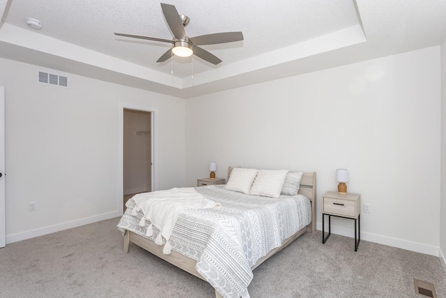 bedroom with light colored carpet, ceiling fan, and a tray ceiling