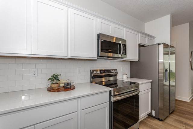 kitchen with a textured ceiling, stainless steel appliances, light wood-type flooring, backsplash, and white cabinetry