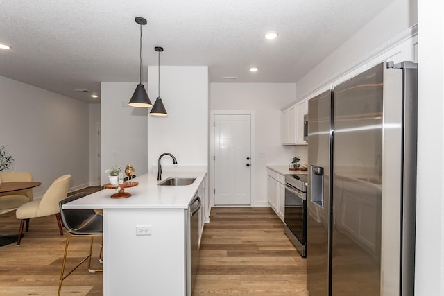 kitchen featuring appliances with stainless steel finishes, hanging light fixtures, sink, light hardwood / wood-style flooring, and white cabinetry