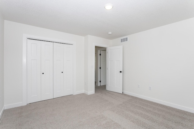 unfurnished bedroom featuring a closet, a textured ceiling, and light colored carpet