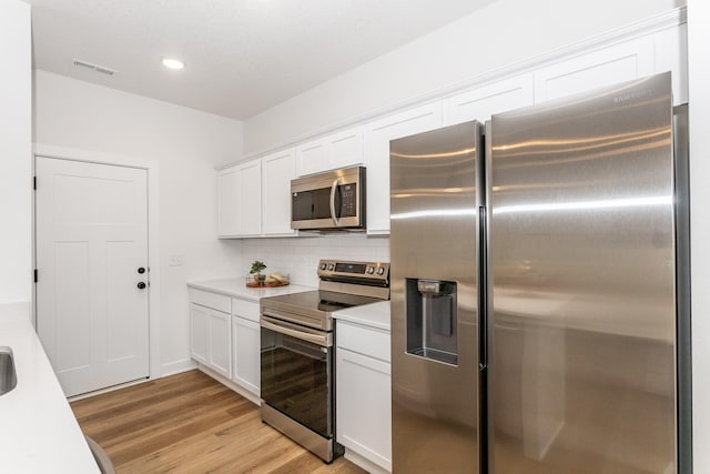 kitchen with stainless steel appliances, white cabinets, tasteful backsplash, and light hardwood / wood-style flooring