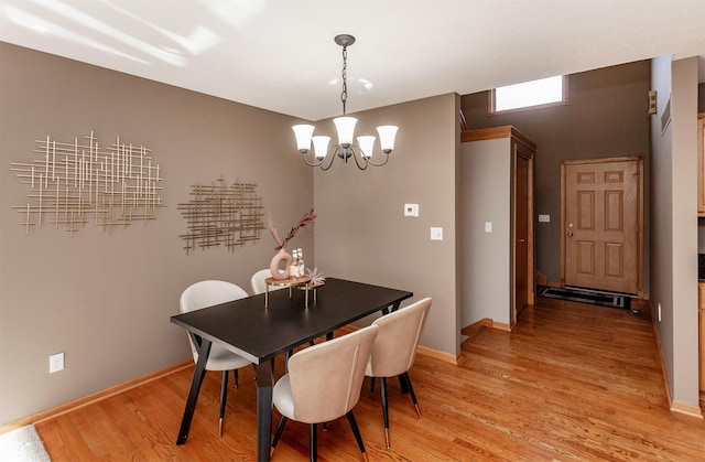 dining area with light wood-type flooring, a notable chandelier, and baseboards