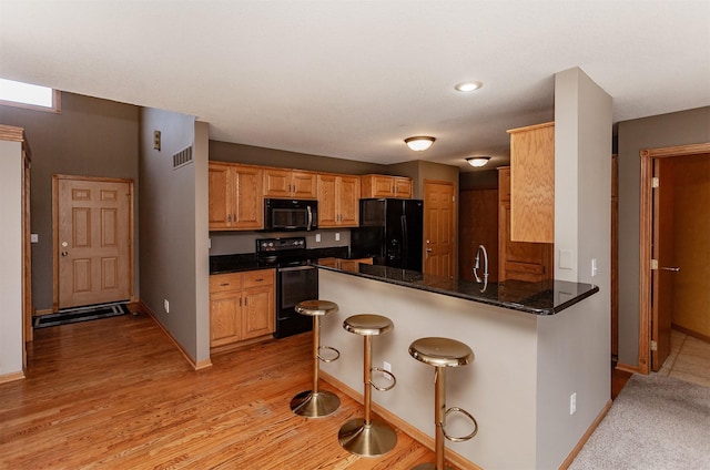 kitchen featuring a breakfast bar area, visible vents, dark stone countertops, a peninsula, and black appliances