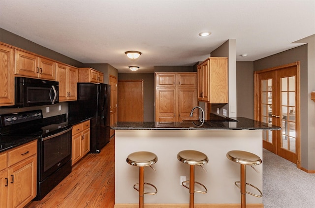 kitchen featuring a peninsula, black appliances, a breakfast bar, and dark stone countertops