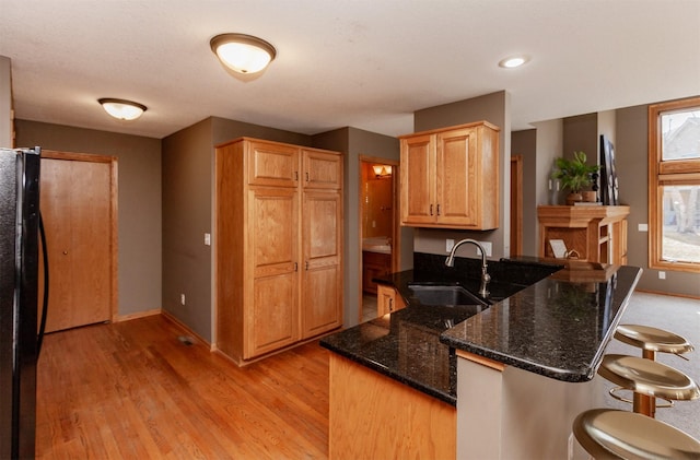 kitchen featuring dark stone counters, a breakfast bar, freestanding refrigerator, a peninsula, and a sink