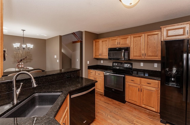 kitchen featuring a sink, black appliances, light wood finished floors, dark stone countertops, and decorative light fixtures