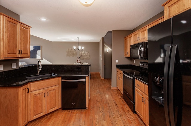 kitchen with hanging light fixtures, light wood-style flooring, a sink, dark stone countertops, and black appliances