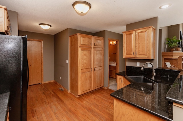 kitchen with a sink, baseboards, freestanding refrigerator, dark stone counters, and light wood finished floors