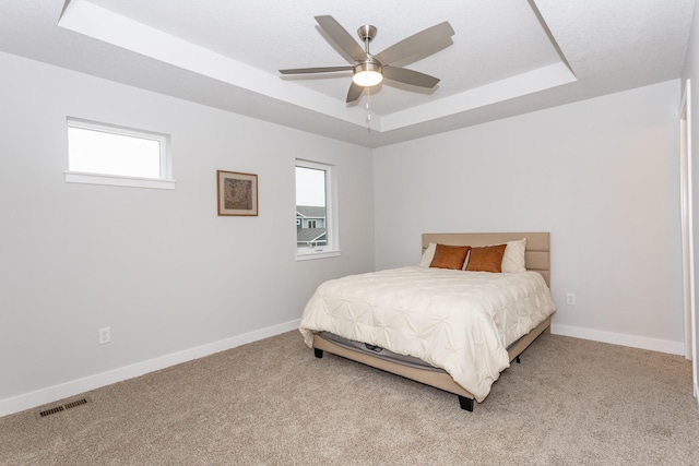 bedroom with a tray ceiling, light carpet, visible vents, and baseboards