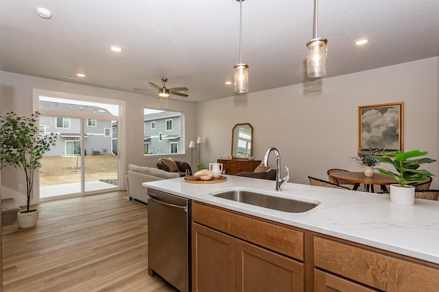 kitchen with brown cabinets, decorative light fixtures, light wood-style flooring, a sink, and dishwasher