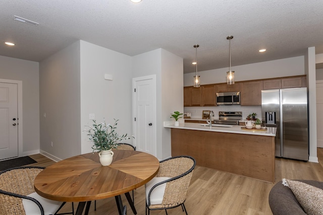 kitchen with stainless steel appliances, light wood-style floors, hanging light fixtures, light countertops, and brown cabinets