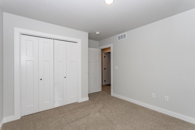 unfurnished bedroom with a textured ceiling, carpet flooring, visible vents, baseboards, and a closet