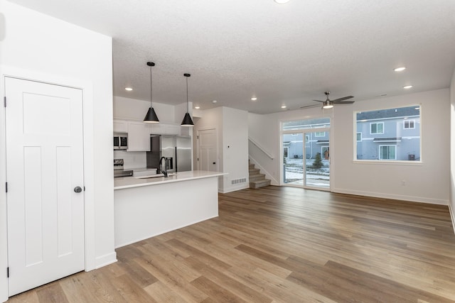 kitchen with hanging light fixtures, stainless steel appliances, ceiling fan, white cabinets, and light hardwood / wood-style flooring